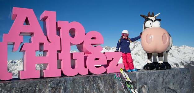 Barn med ski der klapper ko ved Alpe d'Huez skilt på børnevenlig skiferie