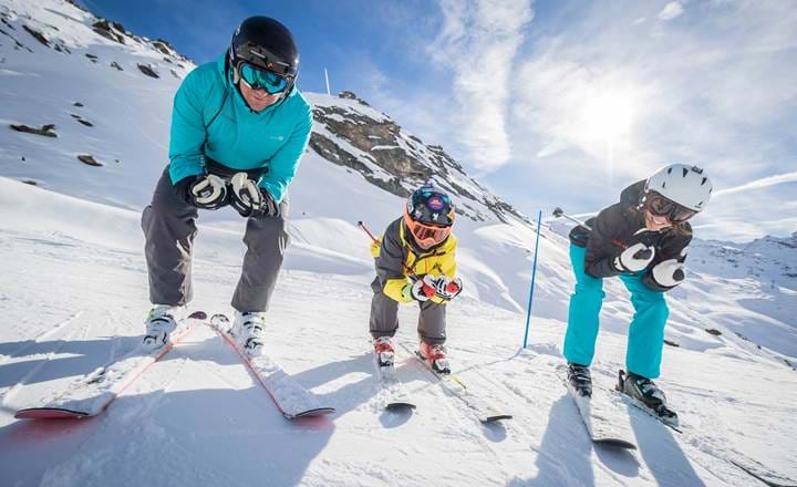 Familie med børn på ski i solskin på hvid piste med smuk udsigt i Val Thorens
