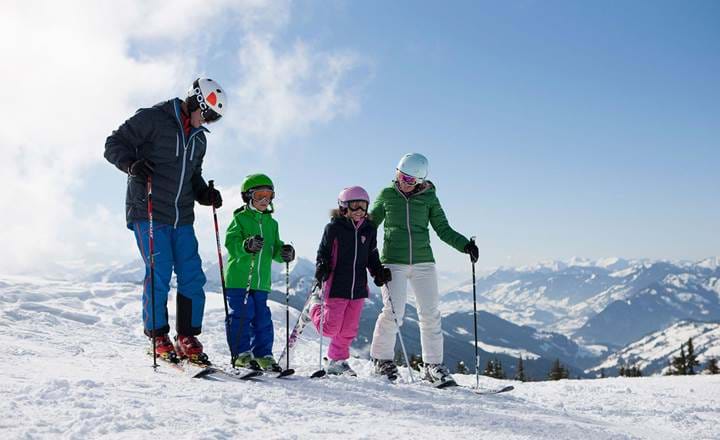 Familie med børn på ski i solskin på hvid piste med smuk udsigt i Wagrain