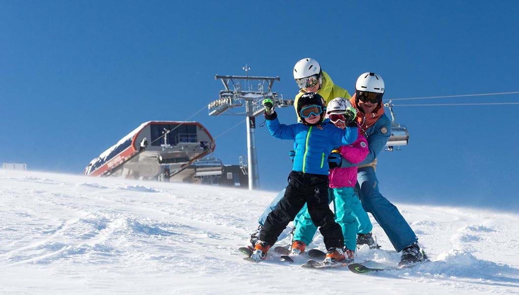 Familie på ski i Lofer med børn under blå himmel ved liften